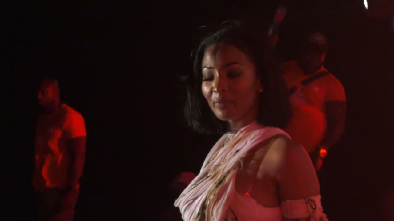 Shenseea sur scène dans une lumière rouge, ses danseurs derrière elle.
