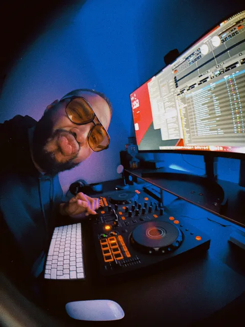 Swan Badol penché sur un contrôleur DJ éclairé au néon bleu, deux écrans de logiciel derrière lui.